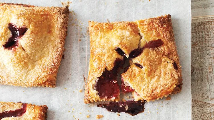 Martha Stewart blackberry-raspberry hand pies with golden flaky crust and jammy berry filling oozing from the vents on parchment paper