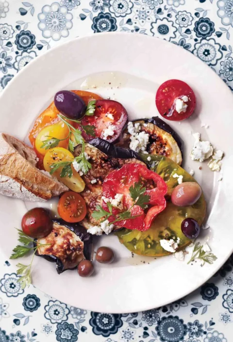 Martha Stewart blistered eggplant with tomatoes, olives and feta on a white plate with parsley and bread