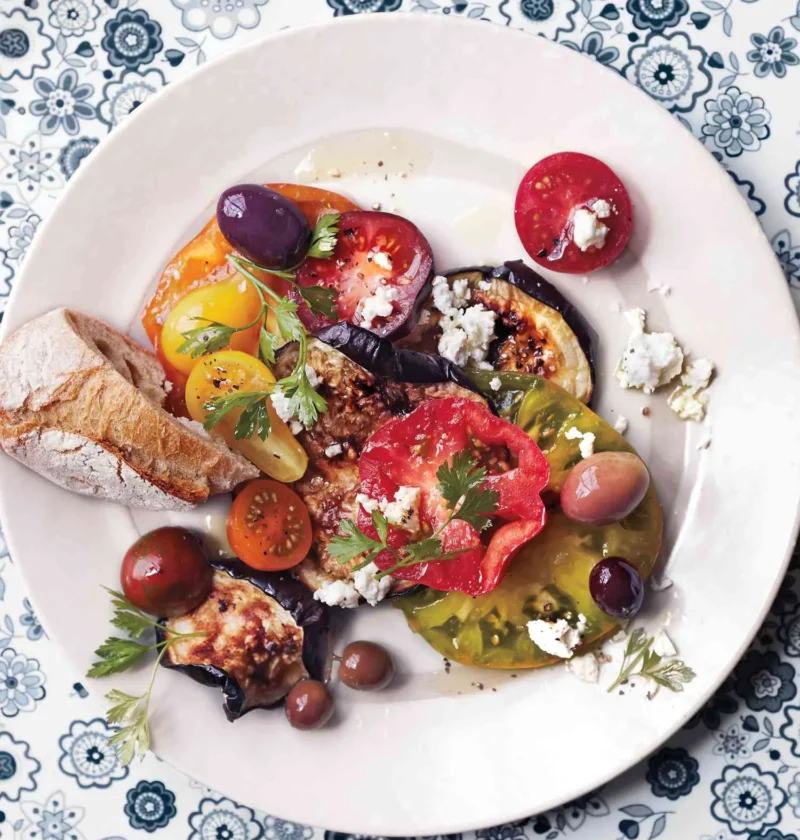 Martha Stewart blistered eggplant with tomatoes, olives and feta on a white plate with parsley and bread