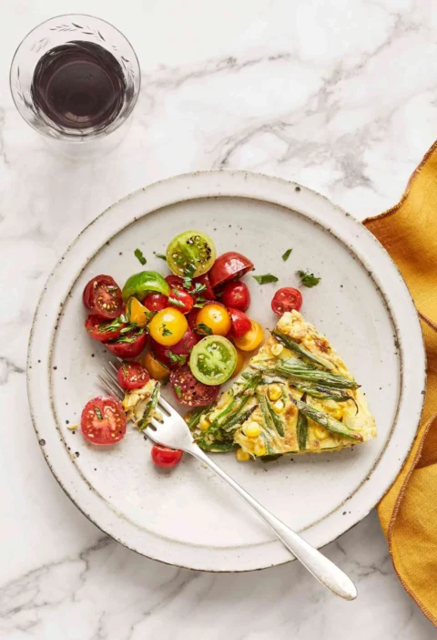 Martha Stewart blistered green-bean and corn frittata slice on a white plate beside a cherry tomato salad