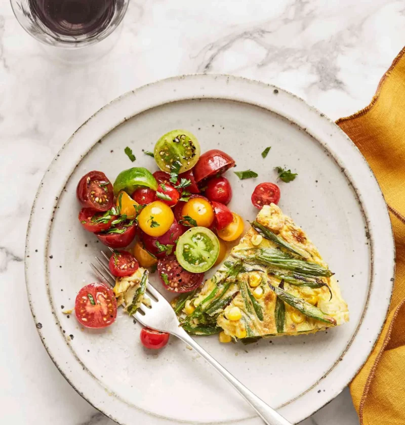 Martha Stewart blistered green-bean and corn frittata slice on a white plate beside a cherry tomato salad