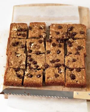 Martha Stewart blondies with chocolate chips and walnuts cut into squares on parchment with a serrated knife