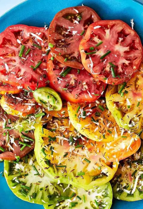 Martha Stewart Bloody-Mary tomato salad with red, yellow and green heirloom tomato slices topped with chives and seeds on a blue plate