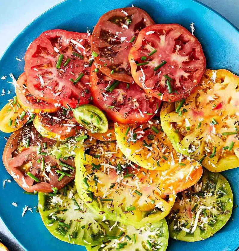 Martha Stewart Bloody-Mary tomato salad with red, yellow and green heirloom tomato slices topped with chives and seeds on a blue plate