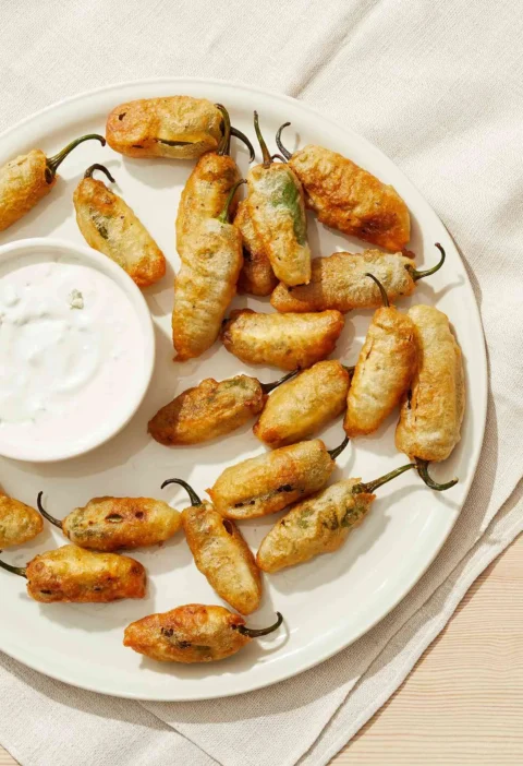 Martha Stewart blue cheese dressing in a small white bowl beside a plate of golden fried jalapeño poppers
