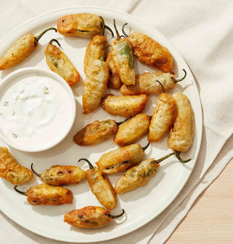 Martha Stewart blue cheese dressing in a small white bowl beside a plate of golden fried jalapeƱo poppers