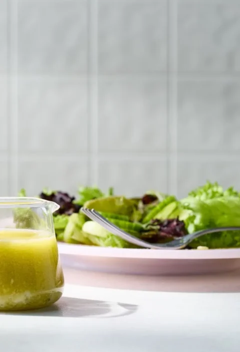 Martha Stewart blue cheese vinaigrette in a small glass pitcher next to a plate of green salad with a fork