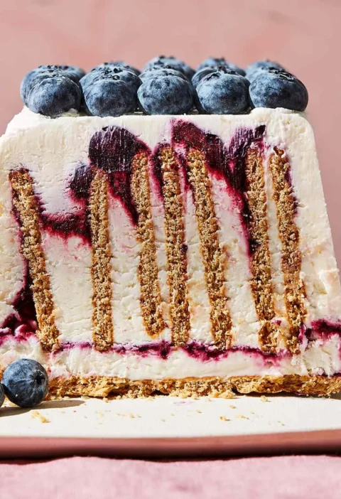 Slice of Martha Stewart blueberry-cheesecake icebox cake showing upright graham crackers, cream cheese layers and blueberry swirls topped with fresh blueberries