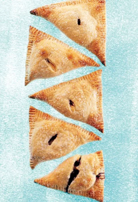 Martha Stewart blueberry-cream cheese hand pies, five golden sugar-topped triangles with vents on a blue background