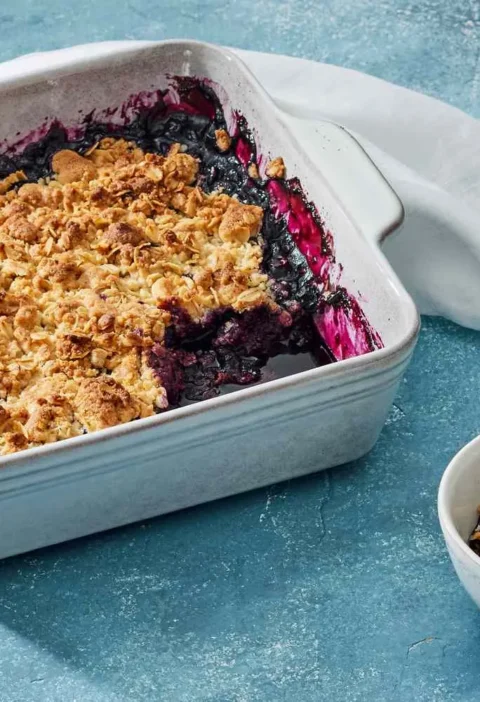 Martha Stewart blueberry crisp with a golden oat topping in a square baking dish next to a small bowl serving