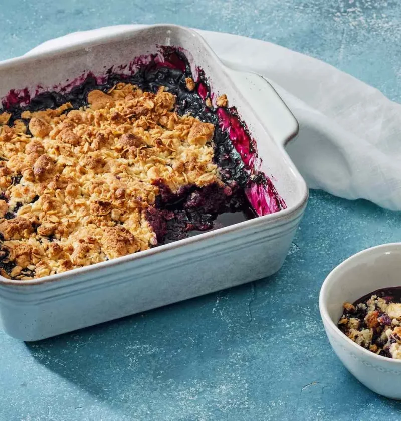 Martha Stewart blueberry crisp with a golden oat topping in a square baking dish next to a small bowl serving