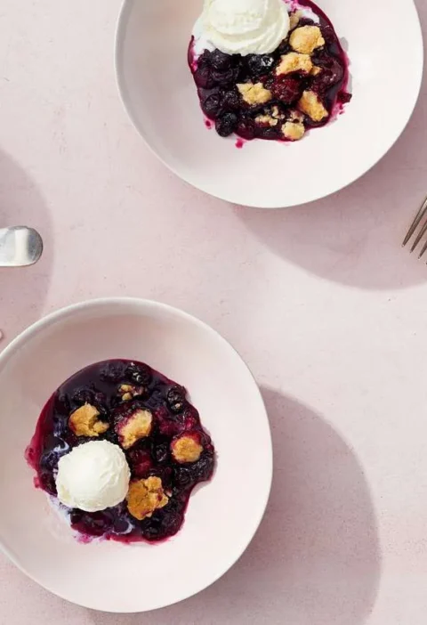 Martha Stewart blueberry crumble in a baking dish and served in white bowls with scoops of vanilla ice cream