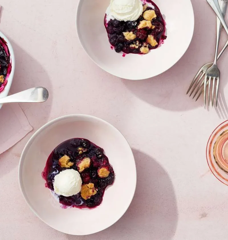 Martha Stewart blueberry crumble in a baking dish and served in white bowls with scoops of vanilla ice cream