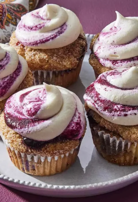 Martha Stewart blueberry cupcakes topped with swirls of cream cheese frosting streaked with blueberry jam on a white plate