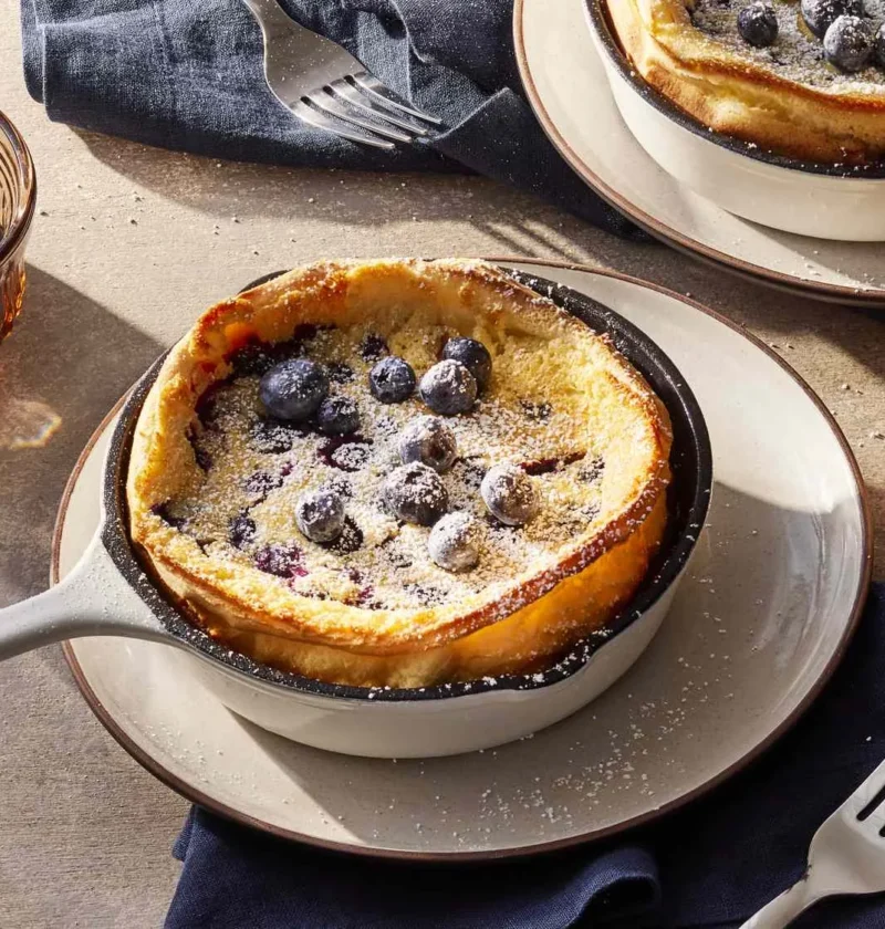 Martha Stewart blueberry Dutch baby pancakes baked in small cast-iron skillets, topped with fresh blueberries and confectioners' sugar