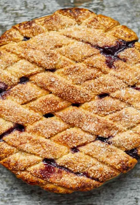 Martha Stewart blueberry lattice pie with a golden sugar-sprinkled woven crust and dark blueberry filling showing through on a weathered wooden surface