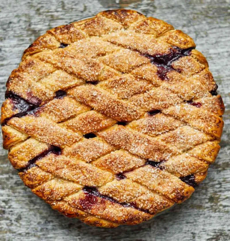 Martha Stewart blueberry lattice pie with a golden sugar-sprinkled woven crust and dark blueberry filling showing through on a weathered wooden surface