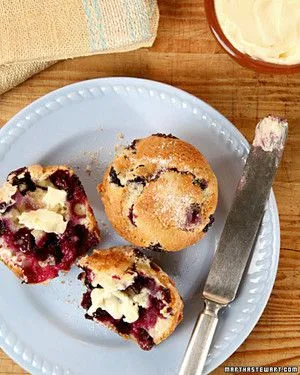 Martha Stewart blueberry muffins, one whole and one split open with melting butter, on a light blue plate with a butter knife