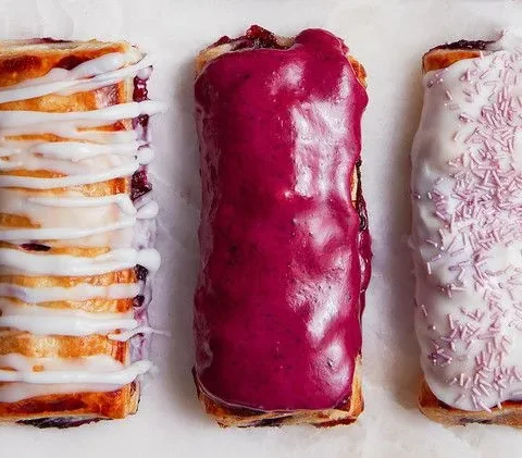 Three Martha Stewart blueberry toaster pastries with white drizzle, purple blueberry glaze and white glaze with purple sprinkles on parchment