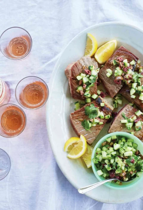 Martha Stewart bluefin tuna with olive, cucumber, and cilantro relish served on an oval platter with lemon wedges next to glasses of rosé