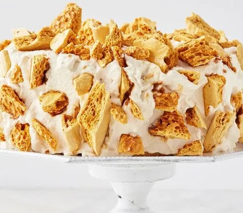 Martha Stewart Blum's coffee crunch cake covered in whipped frosting and golden coffee candy shards on a white cake stand