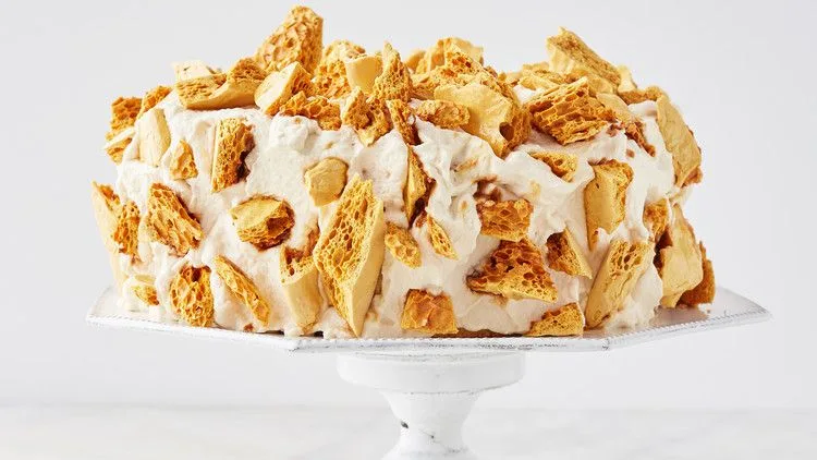 Martha Stewart Blum's coffee crunch cake covered in whipped frosting and golden coffee candy shards on a white cake stand
