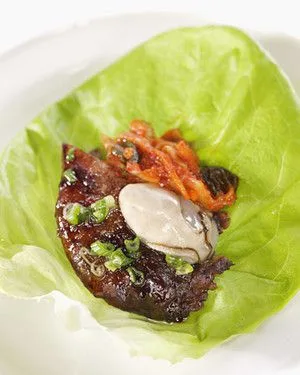 Martha Stewart bo ssam lettuce wrap with glazed pork, a shucked oyster, kimchi and sliced scallions on a Bibb lettuce leaf