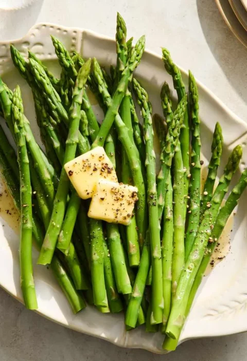 Martha Stewart boiled asparagus on a white platter topped with butter pats, salt and pepper
