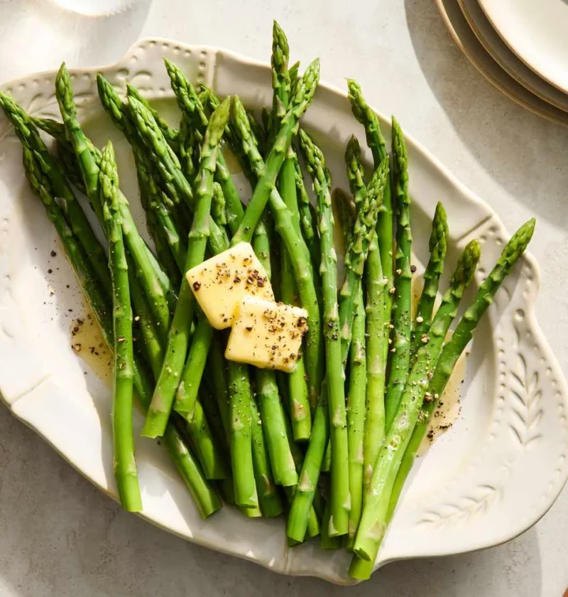 Martha Stewart boiled asparagus on a white platter topped with butter pats, salt and pepper