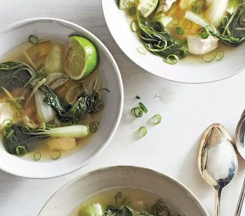 Martha Stewart bok choy and chicken soup in white bowls with lime wedge, sliced scallions and ginger in clear broth