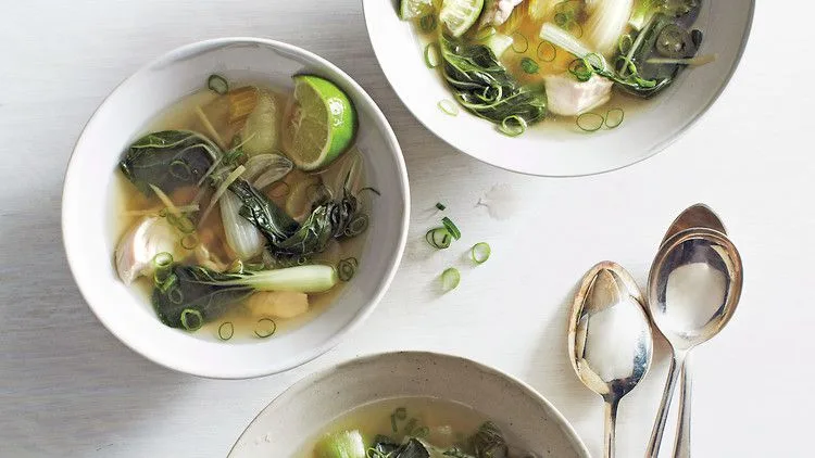 Martha Stewart bok choy and chicken soup in white bowls with lime wedge, sliced scallions and ginger in clear broth