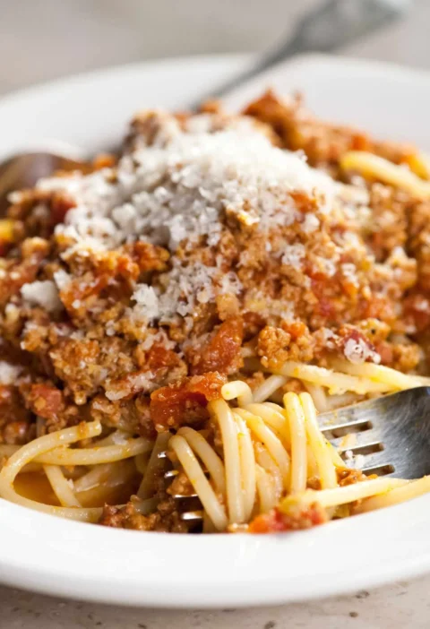 Martha Stewart Bolognese sauce over spaghetti topped with grated cheese on a white plate with a fork