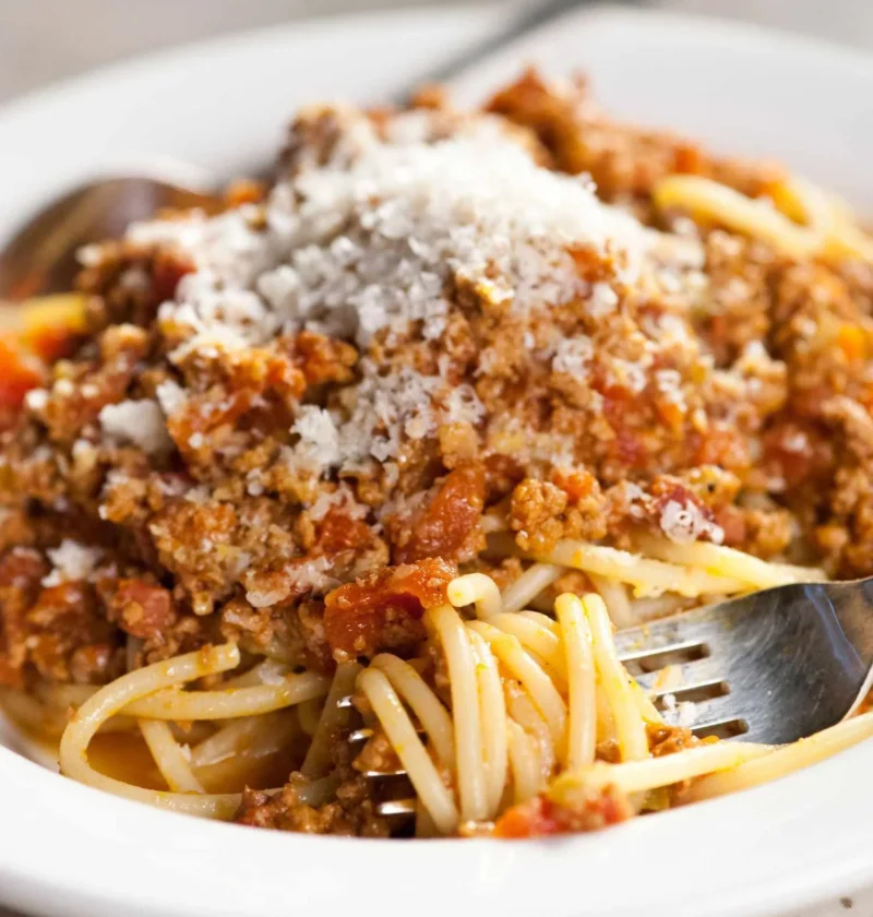 Martha Stewart Bolognese sauce over spaghetti topped with grated cheese on a white plate with a fork