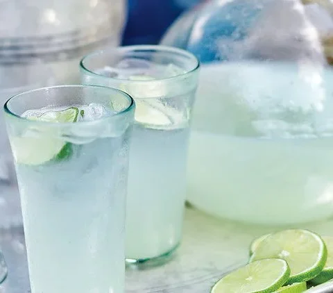 Martha Stewart Bombay Fizz in tall glasses with ice and lime rounds next to a large glass pitcher and sliced limes on a silver tray
