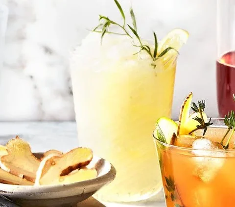Martha Stewart boozy frozen lemonade in a glass garnished with fresh tarragon and a lemon wedge beside a dish of sliced ginger