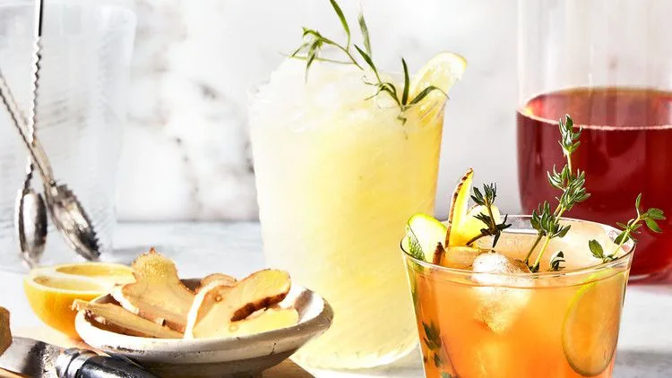 Martha Stewart boozy frozen lemonade in a glass garnished with fresh tarragon and a lemon wedge beside a dish of sliced ginger