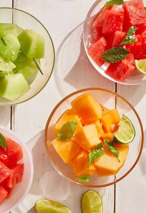 Martha Stewart boozy melon three ways with watermelon, honeydew and cantaloupe cubes in glass bowls with mint, basil, tarragon and lime wedges