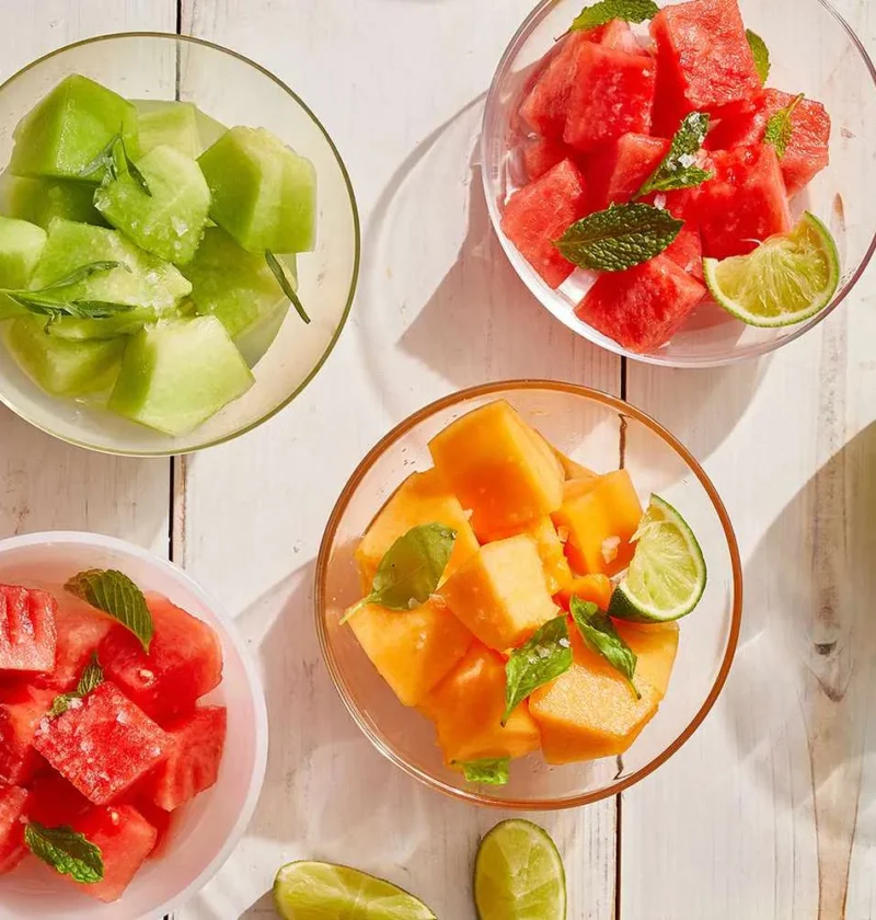 Martha Stewart boozy melon three ways with watermelon, honeydew and cantaloupe cubes in glass bowls with mint, basil, tarragon and lime wedges