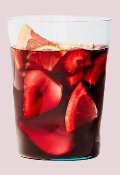 Martha Stewart boozy red sangria in a clear glass with sliced strawberries, grapefruit and lime floating in dark red wine