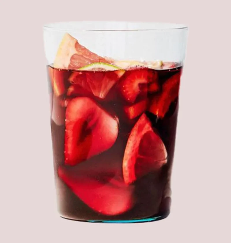 Martha Stewart boozy red sangria in a clear glass with sliced strawberries, grapefruit and lime floating in dark red wine
