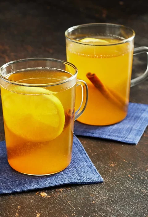 Two glass mugs of Martha Stewart bourbon hot toddy with lemon slices and cinnamon sticks on blue napkins