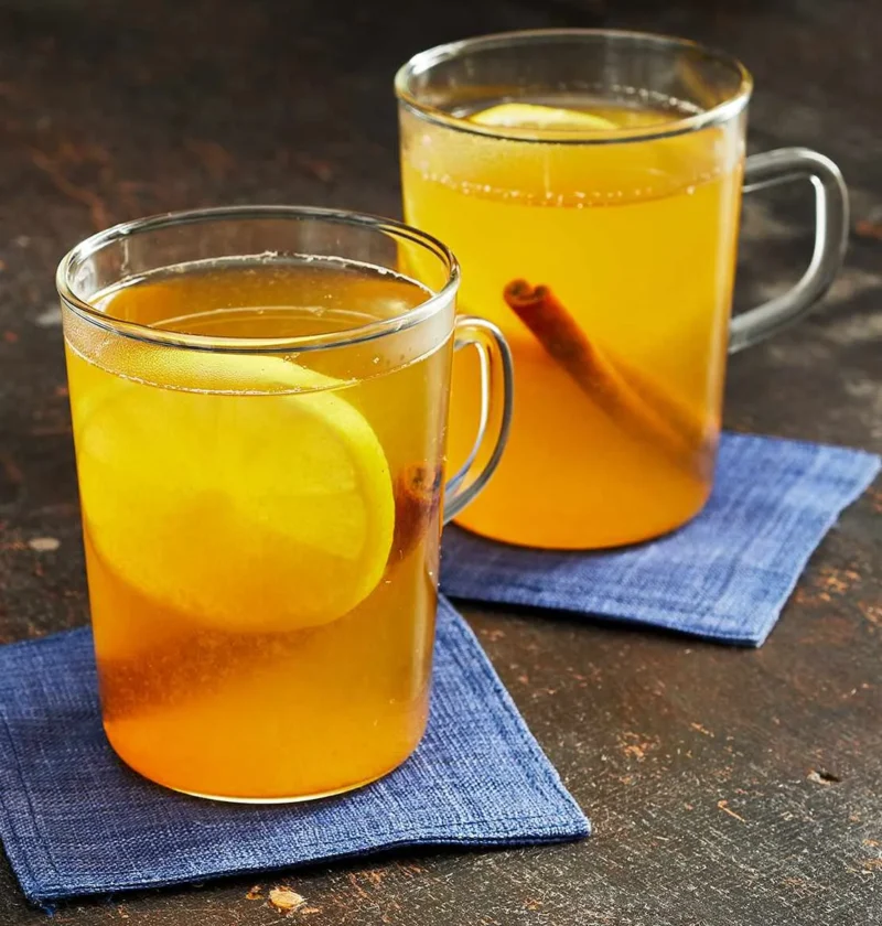 Two glass mugs of Martha Stewart bourbon hot toddy with lemon slices and cinnamon sticks on blue napkins