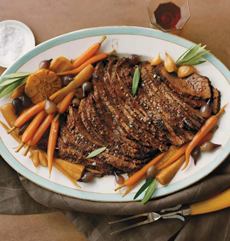 Martha Stewart braised brisket for Passover sliced on an oval platter with roasted baby carrots, parsnips, pearl onions and roasted garlic