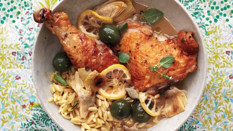 Martha Stewart braised chicken with artichokes, olives and lemon slices served over orzo in a shallow bowl