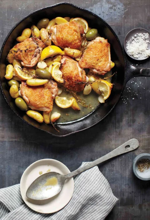 Martha Stewart braised chicken with potatoes, olives, and lemon in a cast iron skillet with golden chicken thighs and lemon slices