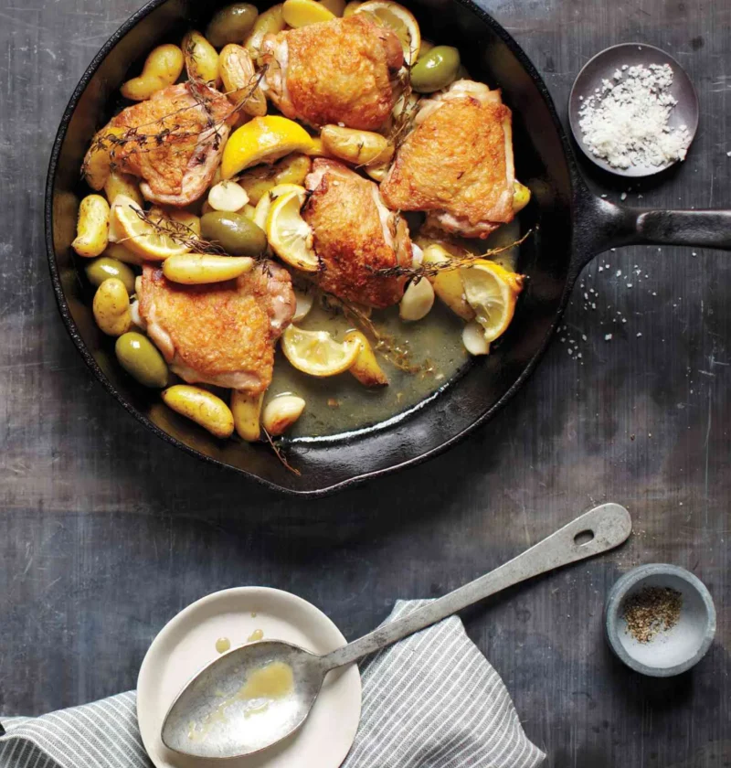 Martha Stewart braised chicken with potatoes, olives, and lemon in a cast iron skillet with golden chicken thighs and lemon slices
