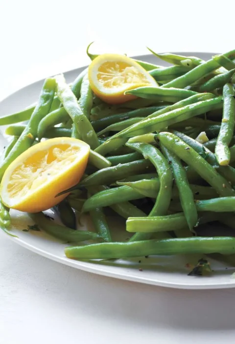 Martha Stewart braised green beans on a white oval platter with lemon halves