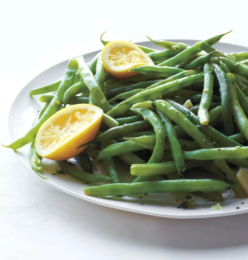 Martha Stewart braised green beans on a white oval platter with lemon halves