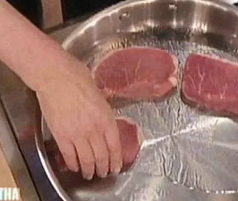 Raw boneless pork chops being placed in a stainless steel skillet for Martha Stewart braised pork chops