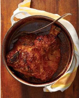 Martha Stewart braised pork shoulder with caramelized onions and jus in a Dutch oven with a serving spoon